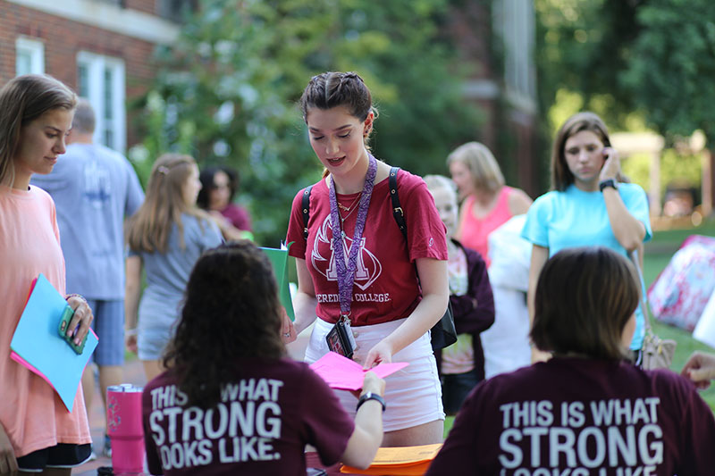 Student with braids and burgundy shirt talking to Meredith staff at a table wearing burgundy "This is what strong looks like" shirts.