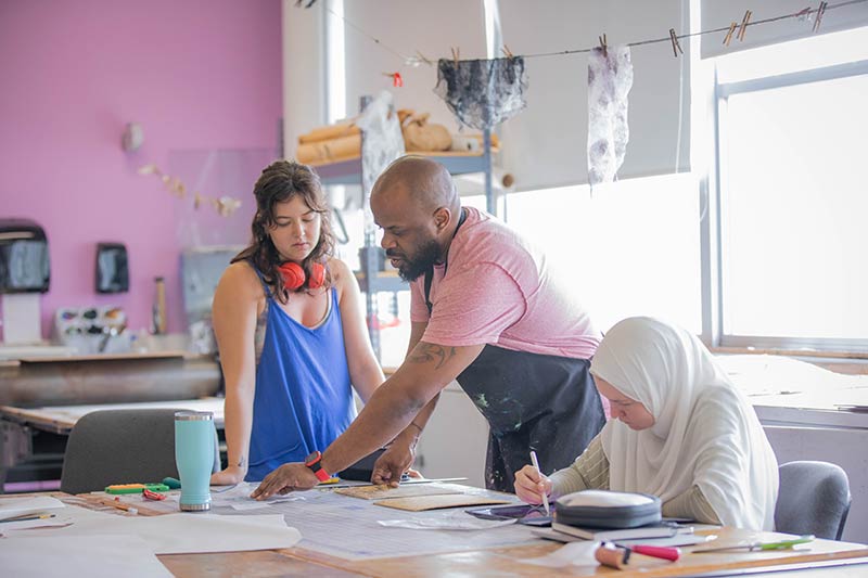 A professor works with two students during a printmaking class.