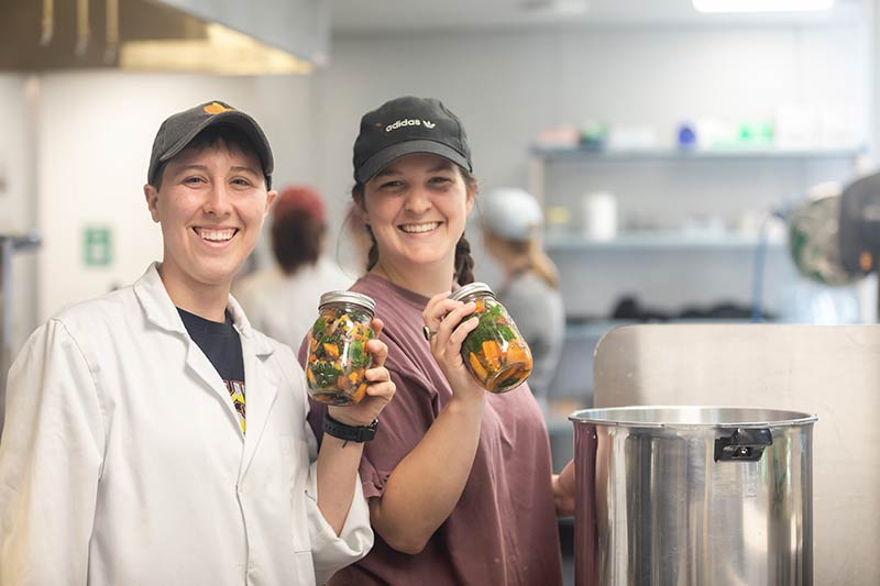 Two students smiling as they hold up cans during an MSN canning lab.