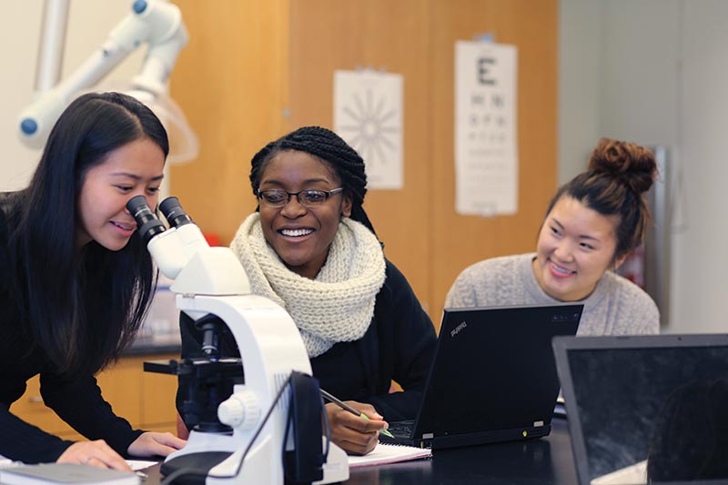 Three students working with a microscope and smiling.