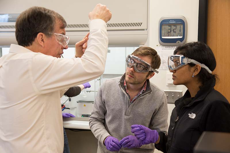 Two students listen intently as a professor explains something.
