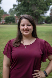  Saiberh Sanderson in red shirt smiling with left hand on hip.